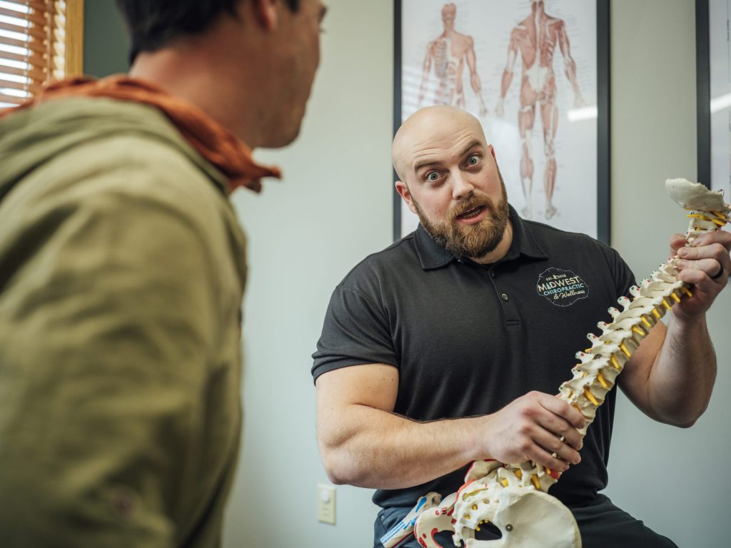 A doctor at Midwest Chiropractic & Wellness explaining a spine model to a patient in an exam room